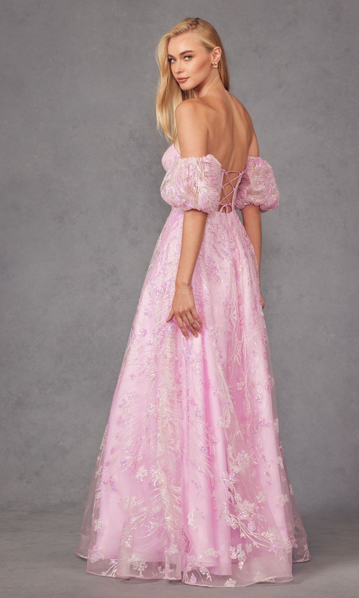 Woman wearing the Puff-Sleeve Strapless Long Glitter Prom Dress 2404, a floor-length gown in pale pink with puff sleeves, a fitted bodice, lace-up back, and shimmering details, standing against a gray background.
